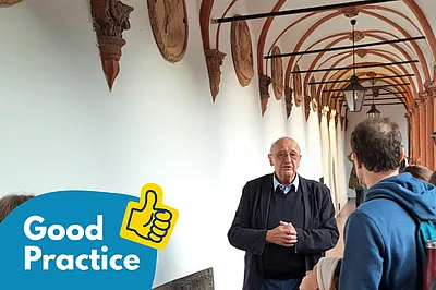 Dr. Gerhard Floßmann spricht zu einer Gruppe, die in einem historischen Gang auf der Schallburg stehen.