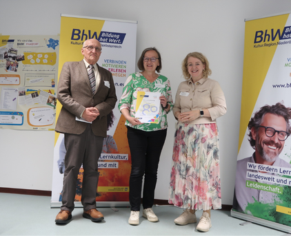 Foto mit 3 Personen, die Person in der Mitte hält eine "80 Jahre BhW" Urkunde.