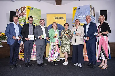 Gruppenbild mit den erwähnten Personen. Im Hintergrund große bunte Würfel mit BhW-Projektinfos und ein Roll der Kulturregion.