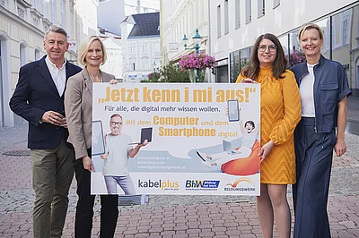Auf dem Foto sind zu sehen: kabelplus-Geschäftsführer Wolfgang Schäffer, Geschäftsführerin des BhW Niederösterreich Therese Reinel, Smartphone-Trainerin Julia Hentschel und Geschäftsführerin des Burgenländischen Bildungswerks Judith Tscheppe. Sie alle halten eine Tafel mit der Aufschrift „Jetzt kenn i mi aus! – Für alle, die digital mehr wissen wollen“ zur Bewerbung von gemeinsam durchgeführten Online-Workshops zu Computer- und Smartphone-Themen. 
