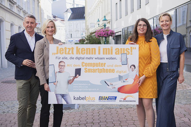 Auf dem Foto sind zu sehen: kabelplus-Geschäftsführer Wolfgang Schäffer, Geschäftsführerin des BhW Niederösterreich Therese Reinel, Smartphone-Trainerin Julia Hentschel und Geschäftsführerin des Burgenländischen Bildungswerks Judith Tscheppe. Sie alle halten eine Tafel mit der Aufschrift „Jetzt kenn i mi aus! – Für alle, die digital mehr wissen wollen“ zur Bewerbung von gemeinsam durchgeführten Online-Workshops zu Computer- und Smartphone-Themen.