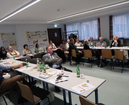 Foto von 3 langen Tischen welche in einer U Form aufgestellt sind. Alle Teilnehmer der Hauptregionskonferenz sitzen an diesen Tischen und schauen nach vorne in die Mitte. Ebenso befinden sich Zettel und Getränke auf den Tischen.