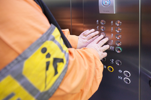 Man sieht den Arm eines blinden Mannes, der die Informationen in einem Lift ertastet - Nahaufnahme der tastbaren Informationen und Braille-Informationen