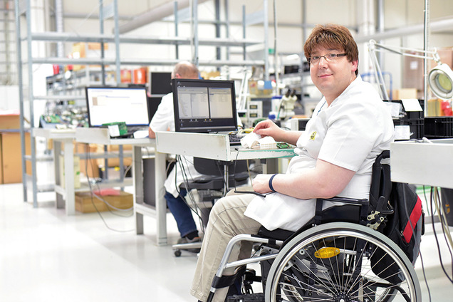 Ein Mann im Rollstuhl bei der Arbeit in einem Industriebetrieb.