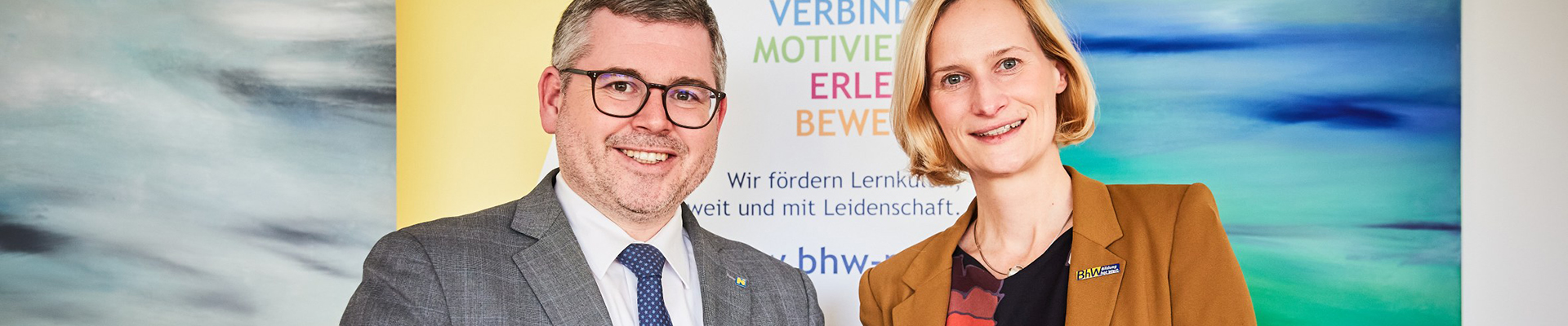 Landesrat Ludwig Schleritzko und BhW Geschäftsführerin Therese Reinel stehen vor einem BhW Rollup und halten jeweils ein Handy in der Hand.